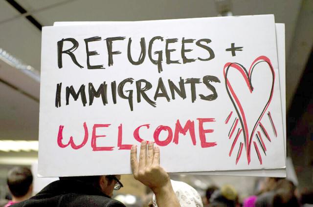 Person holding a sign that says "Refugees and Immigrants Welcome"