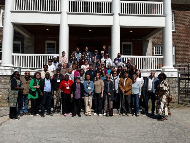 A large group of people stand in front of a brick building with a portico