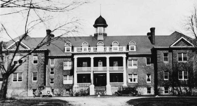 Black and white image of a wide brick building with a portico