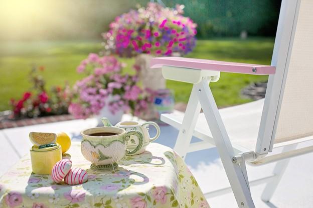 A summer scene of a teacup and snacks on a table next to a lounge chair