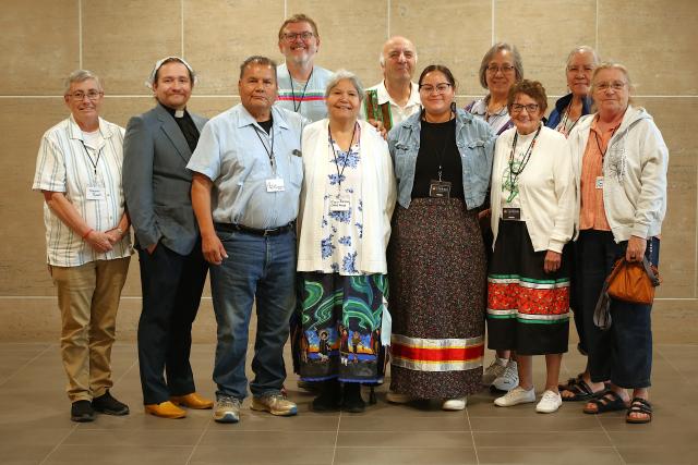 A group of 13 people wearing lanyards pose in a hallway