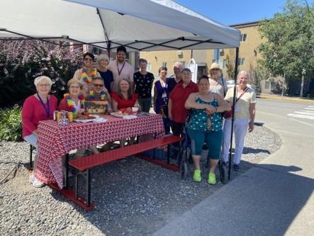 A group of a dozen stand around a brightly decorated picnic table outdoors