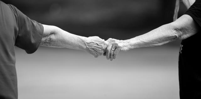 Two older adults reach out to hold each other's hands