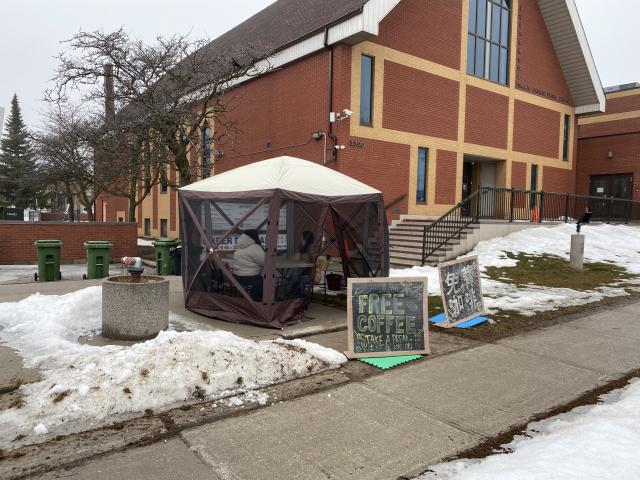 A tent outside a church in which people are drinking coffee at a table
