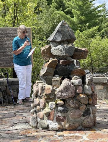 A speaker stands with a microphone in front of a large cairn of rocks