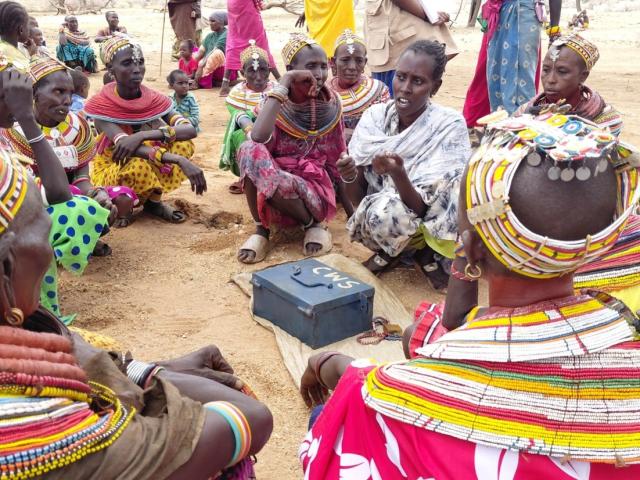 A group of African women sit around a money box in a circle