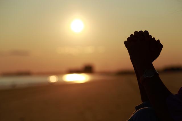 A pair of hands of a person praying in the sun by the sea.