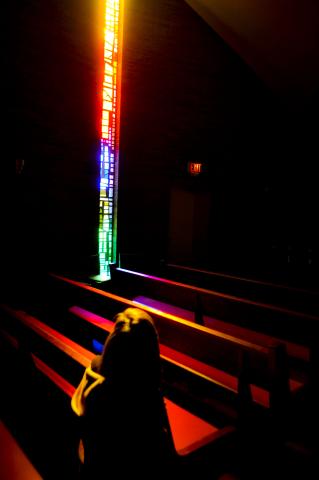 A person sits in a colourful reflection from a stained glass window.