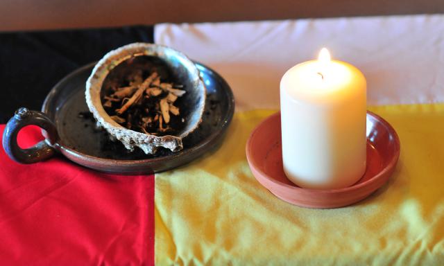 A candle and abalone smudge bowl on a tablecloth making up the four colours of the medicine wheel