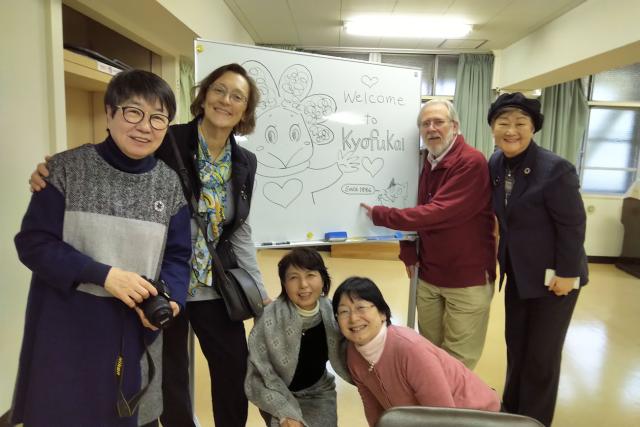 Kyofukai staff (four Japanese women) and United Church representatives (a woman and man) gather about an easel for a photo.