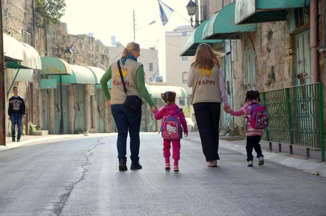 Children on their way to Cordoba School, a Palestinian school in the Israeli-controlled area of Hebron. Two adults in EAPPI vests accompany two children walking down the sidewalk