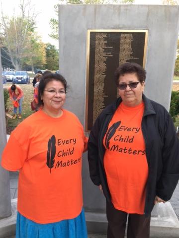 Cynthia Tribe (left) and Martha Albert (right) display their "Every Child Matters" Orange T-shirts at Chippewa of the Thames First Nation ceremony. Two women display their "Every Child Matters" Orange T-shirts at Chippewa of the Thames First Nation ceremony.
