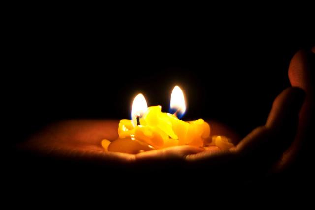 A brown hand holding a yellow candle in the darkness as the candle burns down.
