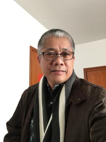 The author, Noel A. Suministrado, a Filipino man with short dark hair with streaks of grey. Wearing glasses and a scarf.