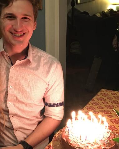 My son Johnny. A young white man standing in a door frame, illuminated by the candles on the cake for his birthday.