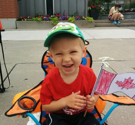 A young boy waves a Canada flag enthusiastically at a Canada Day celebration.