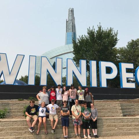 The group of GC43 Pilgrims gather around a huge Winnipeg sign during their visit to the Conference of Manitoba and Northwestern Ontario