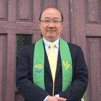Ministry personnel Calin Chun-hong Lau, a man of Chinese descent, stands before a church door in a suit and green stole.