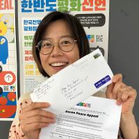 A woman holds up a signed petition and the envelope it was mailed in to Korea