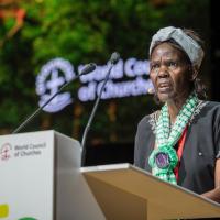 Agnes Abuom stands at a lectern with the World Council of Churches name and logo behind her.