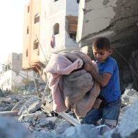 A child carrying a blanket walking through rubble in Gaza