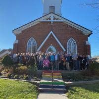 40 people in front of a church door with rainbow-painted steps.