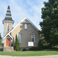 A small white church with a steeple, between two trees.