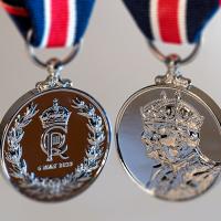 A photograph of both sides of a silver medal featuring the face of King Charles and the King's crest.