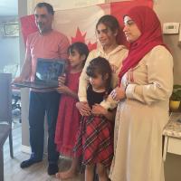 A family of two parents and three young girls holding up a laptop during an online citizenship ceremony.
