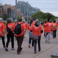 A group of people walking along a pathway wearing orange shirts.