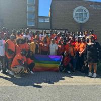 A group of African people, many wearing orange shirts, holding up a pride flag outside of Kitchissippi United Church.