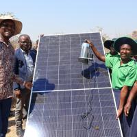 A group of people pose surrounding a solar panel outdoors in Zimbabwe.