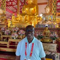 A man in a short-sleeved dress shirt stands smiling in a Buddhist temple.