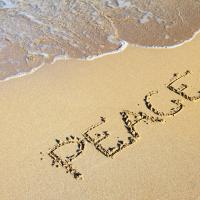 The word "Peace" written in sand on a beach with the shore partially visible.
