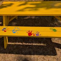 A yellow picnic table with painted handprints on it 
