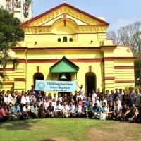 A large group photo of Indian students and educators outside of a yellow building