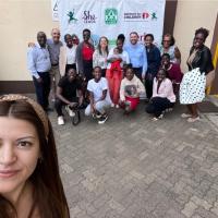 A woman taking a selfie outdoors with a dozen people in the background