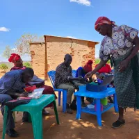 A group of people sitting on plastic chairs and tables outdoors in Kenya