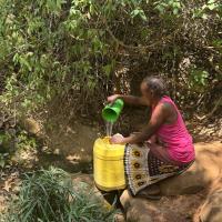 A woman fetching water from a spring with a large plastic jug