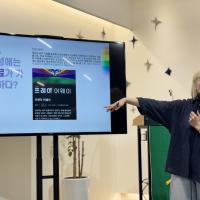 A Korean woman points at a screen with an educational slide on it