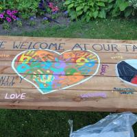 A picnic table with the message "All are welcome at our table" written on it