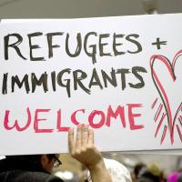 Person holding a sign that says "Refugees and Immigrants Welcome"