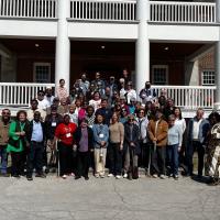 A large group of people stand in front of a brick building with a portico