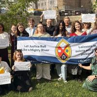 A group of youths hold up signs with slogans calling for climate leadership, as well as a large United Church banner