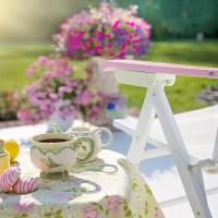 A summer scene of a teacup and snacks on a table next to a lounge chair