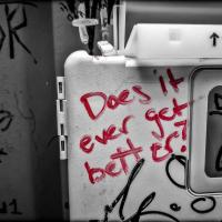 Red graffiti with the phrase "does it ever get better" written in a public toilet