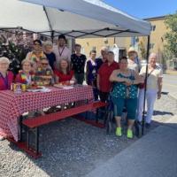 A group of a dozen stand around a brightly decorated picnic table outdoors