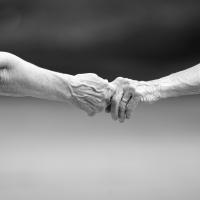 Two older adults reach out to hold each other's hands