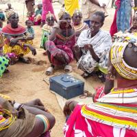 A group of African women sit around a money box in a circle