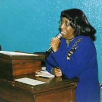 A Black woman in a blue dress speaking into a microphone